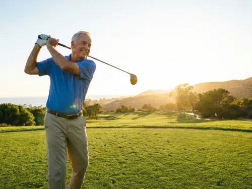 A senior man confidently swinging a golf club on a lush green course after successful knee restoration.