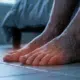 Close-up of bare feet on a floor in a dimly lit bedroom, representing the burning pain and sleepless nights caused by neuropathy.