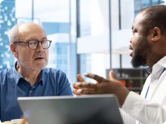 Two men, one older with glasses and one younger with a beard, having a discussion in a modern office, symbolizing a consultation for neurogenic recovery.