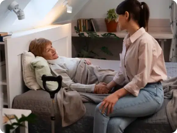 Caregiver holding the hand of an elderly woman in bed, representing compassionate care for patients with progressive neurodegenerative diseases.